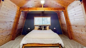 A bedroom with a sloped ceiling, a window, a bed, and two bedside tables. - Dog-friendly 2-story home with large deck, tree views, fireplace, & W/D (Crestline)