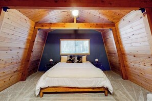 A bedroom with a sloped ceiling, a window, a bed, and two bedside tables. - Dog-friendly 2-story home with large deck, tree views, fireplace, & W/D (Crestline)