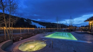 A swimming pool with a hot tub, surrounded by a deck and a fence with lights. - Walk to the Slopes from this Condo with Great Views, Shared Pool, Hot Tub & Sauna (Keystone)