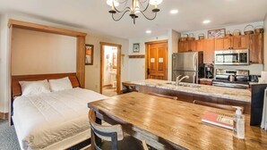 A bedroom with a bed, a wooden dining table, and a kitchen with wooden cabinets and modern appliances. - Walk to the Slopes from this Condo with Great Views, Shared Pool, Hot Tub & Sauna (Keystone)