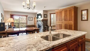 A kitchen with granite countertops, a double sink, wooden cabinets, a chandelier, and a dining area with a table and chairs. - Walk to the Slopes from this Condo with Great Views, Shared Pool, Hot Tub & Sauna (Keystone)