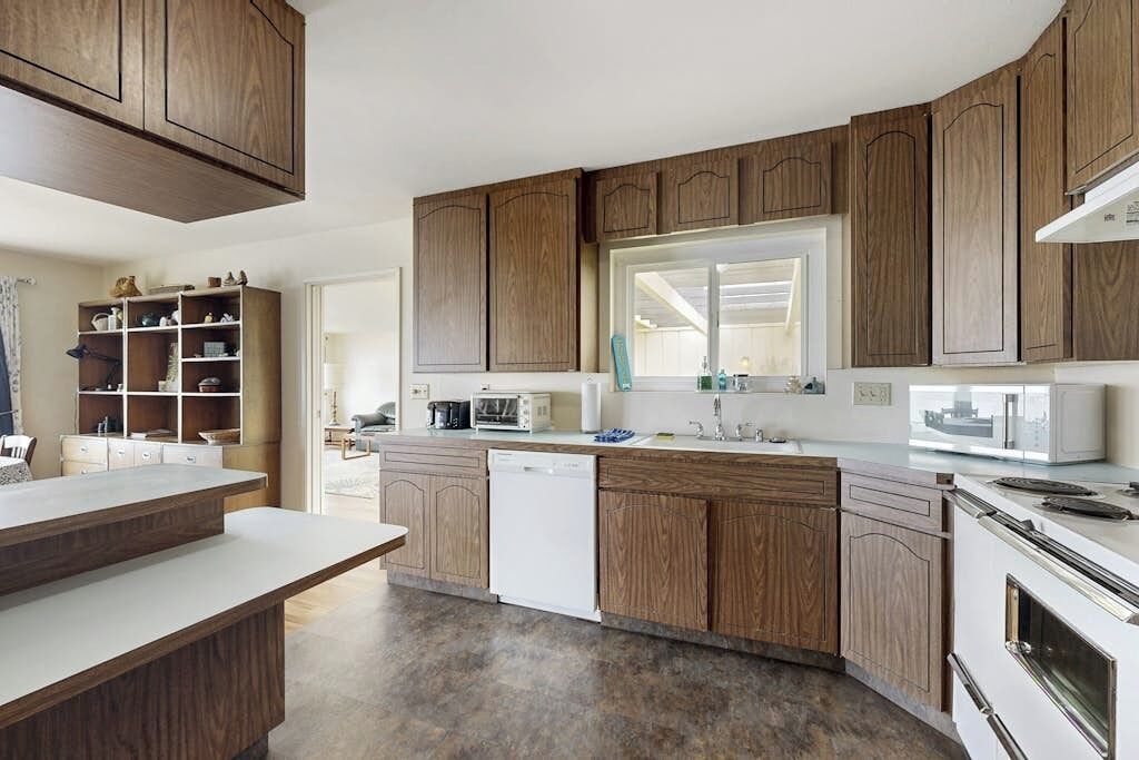 A modern kitchen with wooden cabinets, a built-in dishwasher, and a large window.