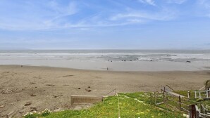A beach with a clear sky, a sandy shore, and a person walking. - Classic waterfront beach house with a furnished deck & ocean views (Cayucos)