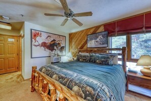 Ein Schlafzimmer mit einem hölzernen Bettgestell, einem Deckenventilator, einem großen Fenster mit Blick auf Bäume und zwei Wandgemälden.