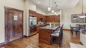 A modern kitchen with wooden cabinets, stainless steel appliances, and a dining area with a bench. - Spacious, walk-to-lift condo with vaulted ceilings, pool, hot tubs & gym (Breckenridge)