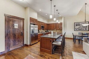 Une cuisine moderne avec des meubles en bois, des appareils électroménagers en acier inoxydable et un coin repas équipé d’une banquette.