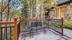 A stone building with a stone facade, a wooden deck with a metal railing, and a bench. - Spacious, walk-to-lift condo with vaulted ceilings, pool, hot tubs & gym (Breckenridge)