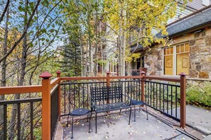 Un bâtiment en pierre avec une façade en pierre, une terrasse en bois dotée d’une rambarde en métal et un banc.