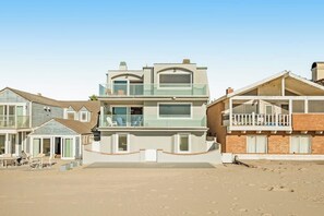 Una propiedad frente a la playa de varios pisos, con balcones, un patio cubierto y una zona de arena.