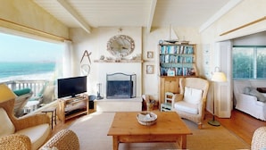 Una sala de estar acogedora con televisor, chimenea, estantería y mobiliario de mimbre, con vistas a un paisaje pintoresco.