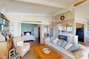 Ein gemütliches Wohnzimmer mit Sofa, Sessel und Couchtisch, ein Schlafzimmer mit Bett und Nachttisch sowie eine Küchenzeile mit Arbeitsplatte und Geräten.