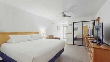 A hotel room with a bed, a desk with a computer, a TV, a ceiling fan, and a mirror.