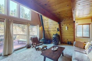 Ein gemütliches Blockhaus-Interieur mit Kamin, Holzwänden, einer Essecke und Blick durch große Fenster.
