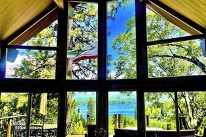 Ein Zimmer mit großen Fenstern und Blick auf einen See und Bäume.