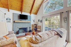 Ein Wohnzimmer mit Kamin, Holzboden und großen Fenstern.