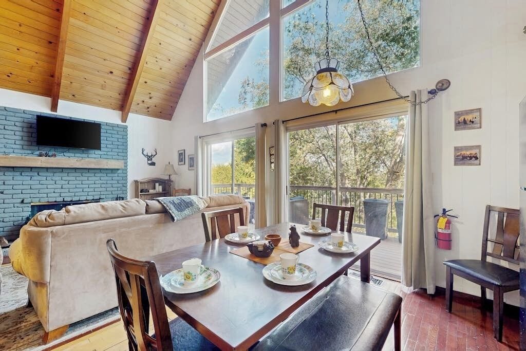 A dining area with a wooden table set for four, a sofa, and a TV mounted on a brick wall.