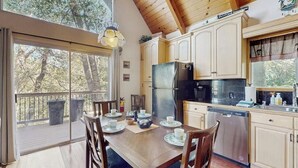 Una cocina con armarios de madera, un refrigerador negro y una mesa de comedor lista para cuatro comensales.