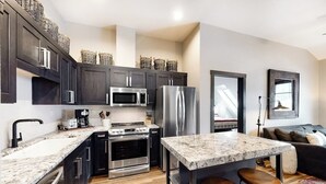 A modern kitchen with dark cabinets, stainless steel appliances, a marble countertop, and a bar area. - Modern, in-town condo with pool & hot tubs - walk to lifts & Main Street (Breckenridge)