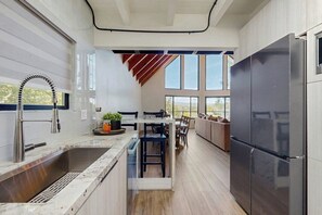A modern kitchen with a large island, a built-in refrigerator, and a dining area with a view. - Modern chalet w/expansive deck, gas grill, & game room - close to lake & town (Lake Arrowhead)