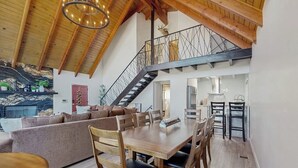 Un loft amplio con techo alto, una mesa de comedor de madera, una escalera y una zona de estar acogedora.