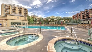 Ett hotell med ett poolområde som har bubbelpooler och solstolar, och som är omgivet av byggnader och berg.
