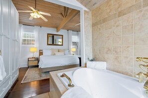 A bedroom with a large bed, a bathtub, and a ceiling fan.