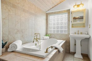 A bathroom with a freestanding bathtub, a pedestal sink, and a window with a decorative grid pattern.