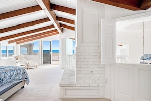 A bedroom with a bed, a white brick fireplace, and a balcony with a view of the ocean. - Oceanfront Home with Giant Picture Windows, Gas Fireplace, and Free WiFi (Oxnard)