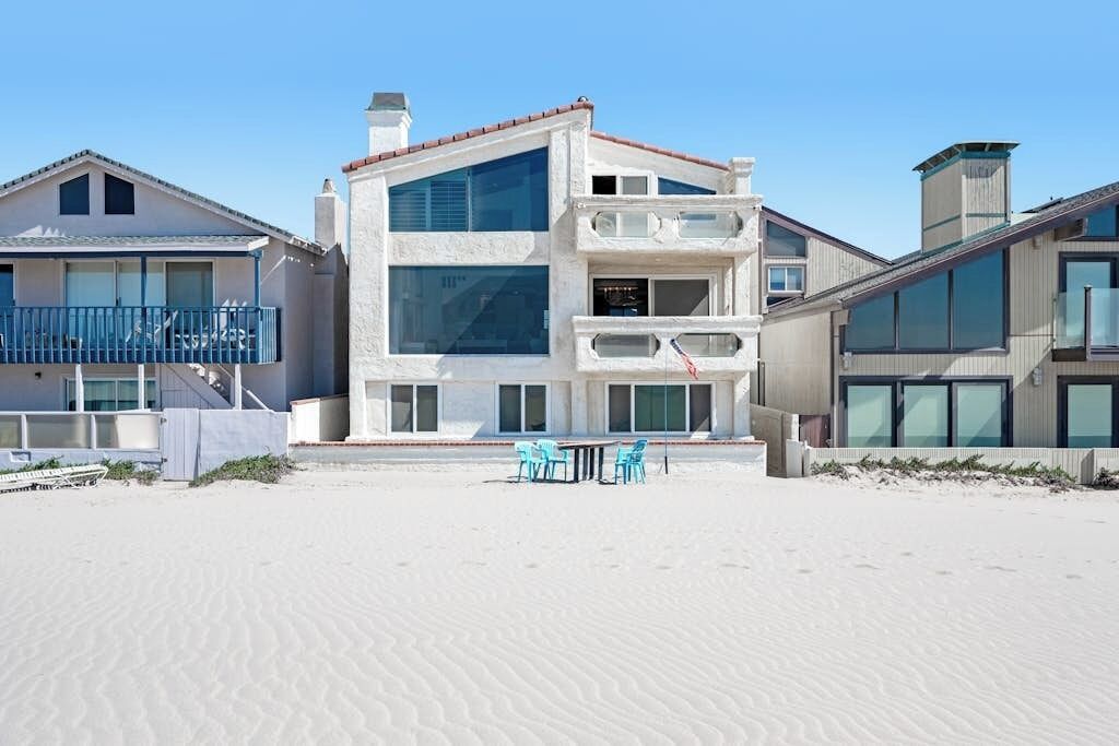 A beachfront property with a multi-story building, a balcony, and a sandy beach area.