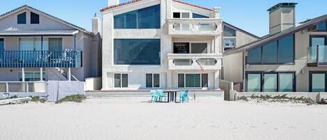 A beachfront property with a multi-story building, a balcony, and a sandy beach area.