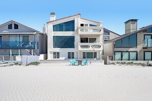 A beachfront property with a multi-story building, a balcony, and a sandy beach area. - Oceanfront Home with Giant Picture Windows, Gas Fireplace, and Free WiFi (Oxnard)