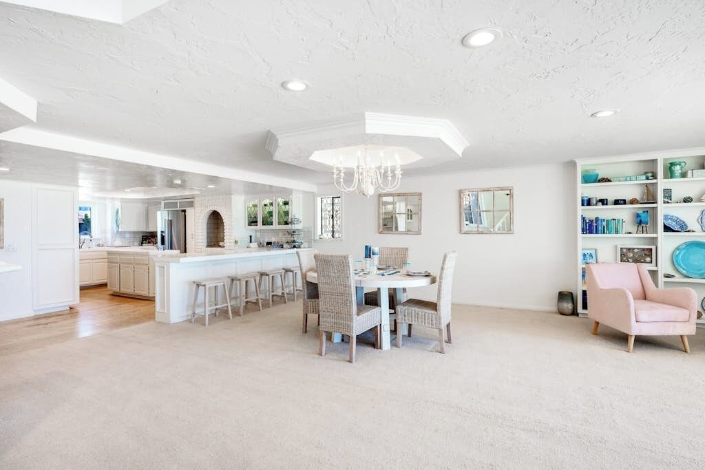 A spacious kitchen with a central island, a dining area with a chandelier, and a living space with a bookshelf.