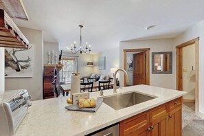 A kitchen with a large island, a chandelier, wooden cabinets, and a dining area in the background. - Cozy Ski-In/Ski-Out Condo with WiFi, Pool, & Hot Tub (Keystone)