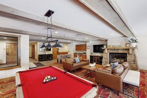 A spacious living area with a pool table, sofas, a fireplace, and a kitchen in the background. - Cozy Ski-In/Ski-Out Condo with WiFi, Pool, & Hot Tub (Keystone)