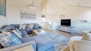 A modern living room with a sectional sofa, a flat-screen TV, and a minimalist design. - Stunning ocean-view home with W/D, sauna, tennis court, & patio - beach access (Moss Landing)
