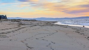 A beach with footprints, a building, and a sunset. - Stunning ocean-view home with W/D, sauna, tennis court, & patio - beach access (Moss Landing)