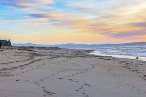 Ein Strand mit Fußspuren, einem Gebäude und einem Sonnenuntergang.