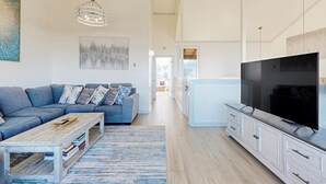 A modern living room with a sofa, coffee table, TV, and artwork. - Stunning ocean-view home with W/D, sauna, tennis court, & patio - beach access (Moss Landing)