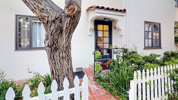 A white building with a tree in front, a white picket fence, and a door with a black frame. - Classic beach suite 1 block to ocean - fireplace, lovely patio, near downtown (Santa Barbara)