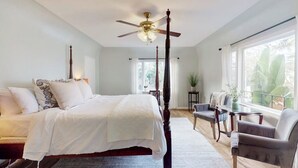 A bedroom with a four-poster bed, a ceiling fan, a window with curtains, a small table, and a chair. - Classic beach suite 1 block to ocean - fireplace, lovely patio, near downtown (Santa Barbara)