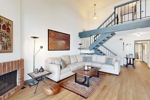 Un salón amplio con un sofá blanco, una mesa de centro, chimenea, una escalera y obras de arte en las paredes.
