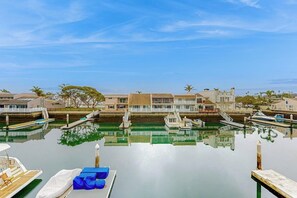Una marina con barcos amarrados, cielo despejado y edificios residenciales al fondo.