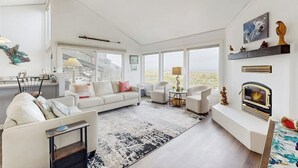 A spacious living room with a fireplace, white furniture, and large windows.