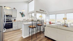 A modern kitchen with a central island, bar stools, a white sofa, and large windows.