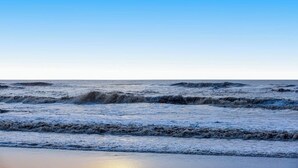 A beach with waves, a clear sky, and a calm sea.