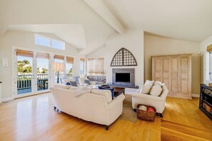 A spacious living room with a fireplace, white sofas, and a large wooden cabinet. - Beach villa with ocean views, internet & washer/dryer - snowbird-friendly (Summerland)