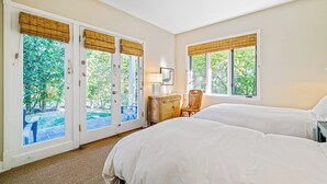 Ein Hotelzimmer mit zwei Betten, einem Schreibtisch, einem Stuhl und großen Fenstern mit Jalousien.