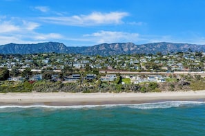 Eine Wohngegend an der Küste mit Häusern, einem Strand und Bergen im Hintergrund.