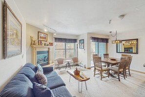 Ein Wohnzimmer mit einer Couch, einem Kamin, einem Essbereich mit Tisch und Stühlen sowie großen Fenstern.
