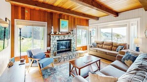 A cozy living room with a stone fireplace, wooden ceiling beams, a sofa, and a coffee table. - Panoramic Ocean and Sunset Views with EV Charging available (Cambria)